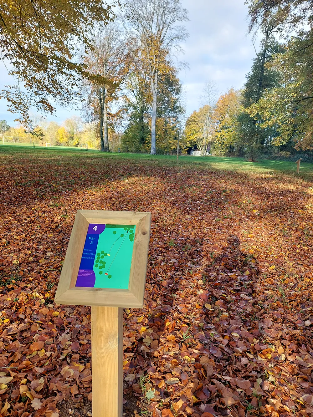 photo d'un panneau arboretum devant un parc rempli de feuilles au sol